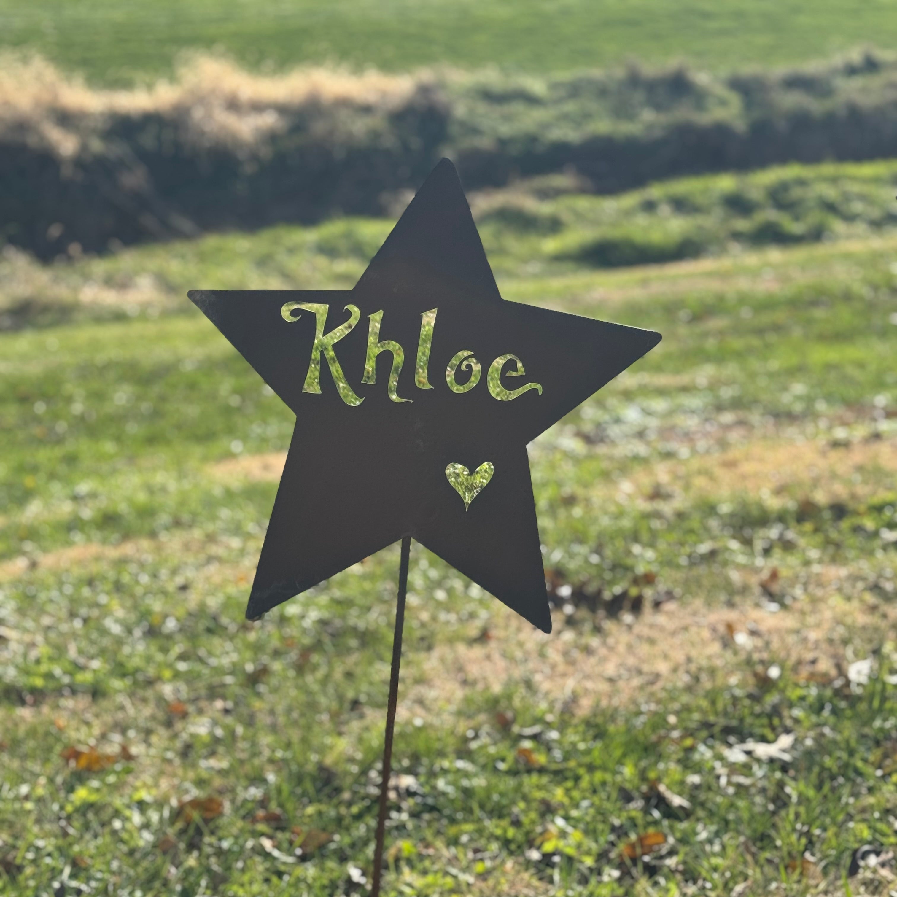 Star-shaped garden sign with 'Khloe' written on it in a grassy field