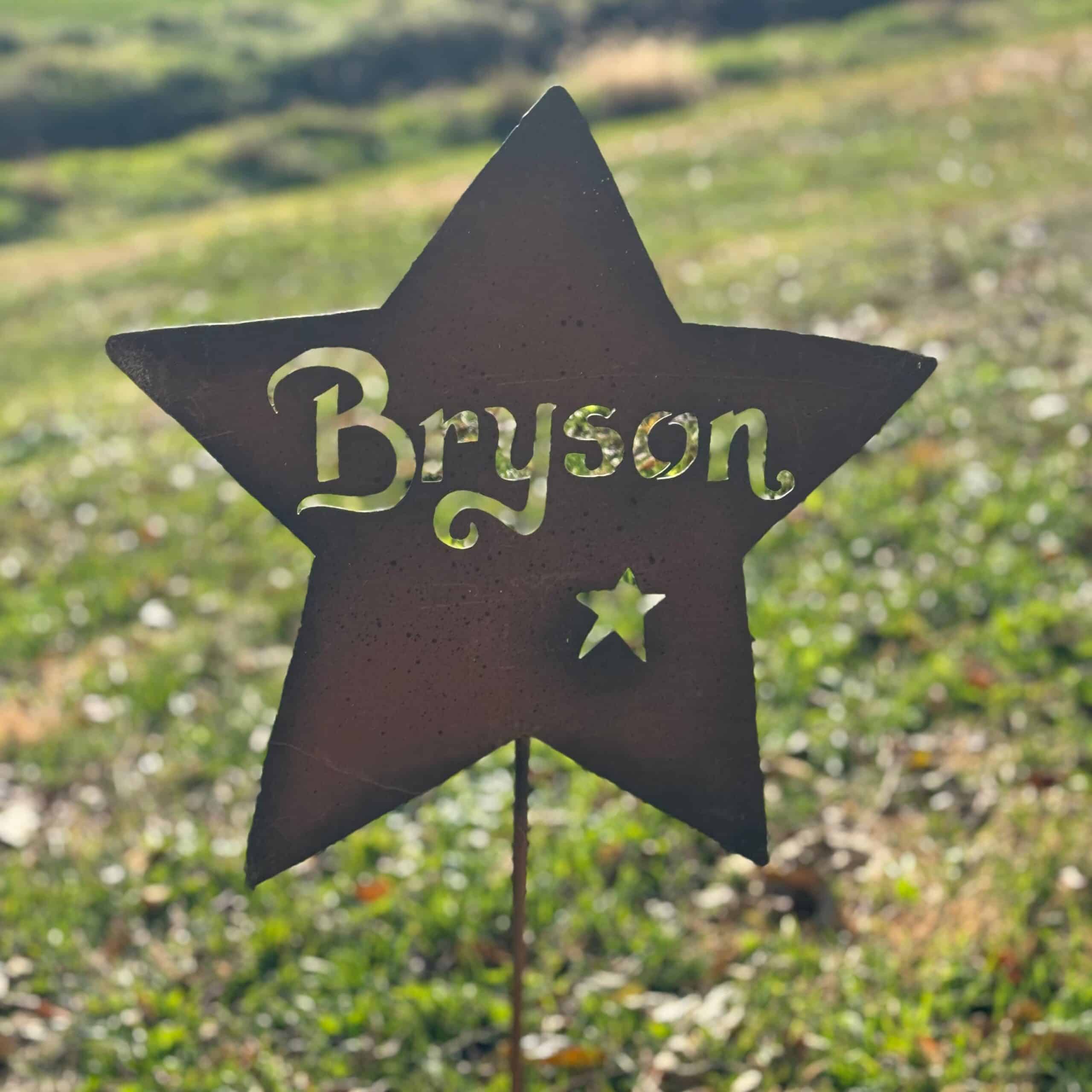 The Handcrafted Metal Name Star – Personalized Outdoor Garden Art features "Bryson" and a small cutout star, shaped like a star, displayed on a sunlit grassy field.