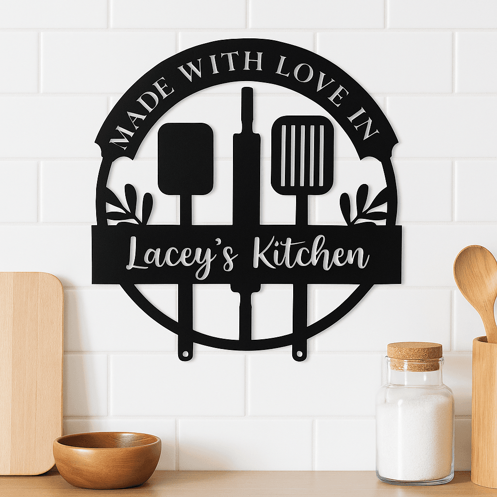 The Custom Metal Wall Sign - Kitchen Utensils hangs on a white tiled wall, displaying "MADE WITH LOVE IN Laceys Kitchen" with utensil and leaf designs. Below, wooden utensils, a sugar jar, and a small wooden bowl are arranged on the counter.