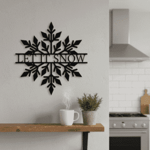 A black snowflake wall decoration with the words LET IT SNOW hangs on a light gray wall above a wooden shelf holding a steaming white mug and a potted plant. A modern kitchen is visible in the background.